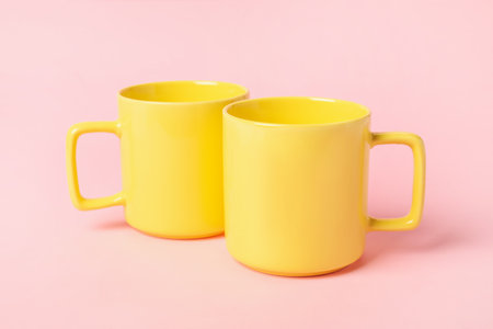 Two yellow ceramic mugs on pink backgroundの写真素材