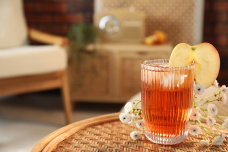 Glass of tasty cider and flowers on wicker table in room, space for text. Relax at homeの写真素材