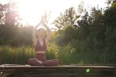 Beautiful woman practicing Padmasana on yoga mat on wooden pier near pond, space for text. Lotus poseの写真素材