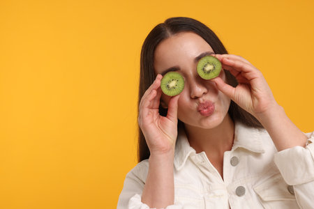 Woman covering eyes with halves of kiwi on yellow background, space for textの写真素材