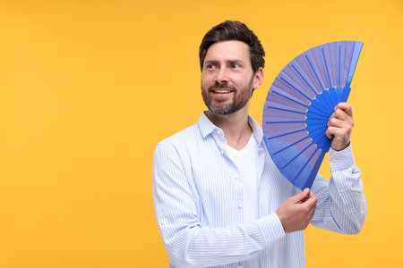 Happy man holding hand fan on orange background. Space for textの写真素材