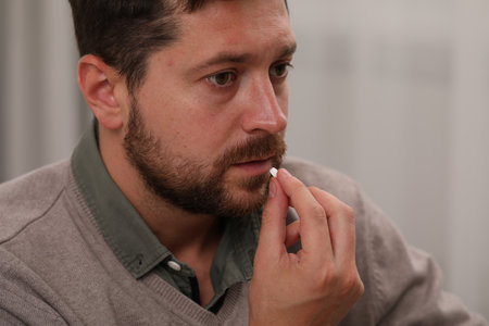 Depressed man taking antidepressant pill on light background, closeup