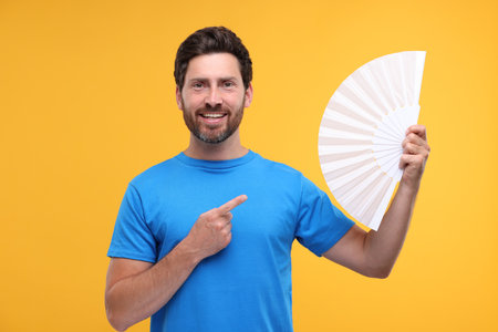 Happy man holding hand fan on orange backgroundの写真素材