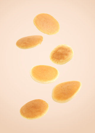 Tasty fresh pancakes falling on beige backgroundの写真素材