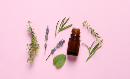 Bottle of essential oil, different herbs and lavender flowers on pink background, flat layの写真素材