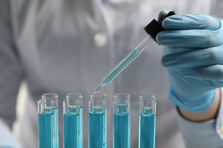 Scientist dripping liquid from pipette into test tube in laboratory, closeup