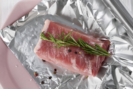Aluminum foil with raw meat, rosemary and spices on white table, top viewの写真素材