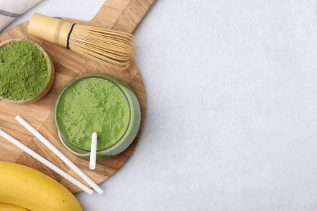 Glass of tasty matcha smoothie, powder, bamboo whiskey and straws on light table, flat lay. Space for textの写真素材