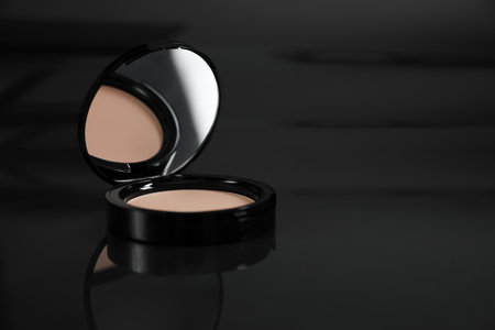 Open face powder on black mirror surface, closeup. Space for text