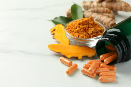 Aromatic turmeric powder, pills and raw roots on white marble table, closeup. Space for textの写真素材