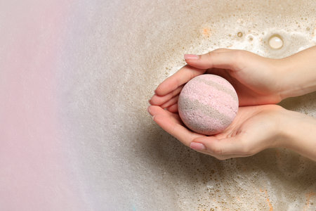 Woman holding bath bomb over water with foam, top view. Space for textの写真素材