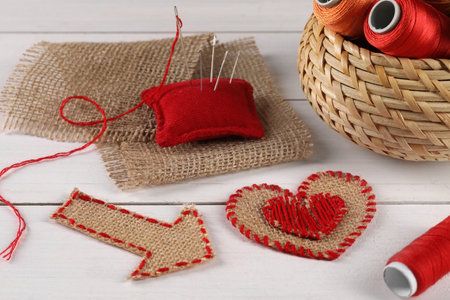 Pieces of burlap fabric, spools of threads, pincushion and needles on white wooden table