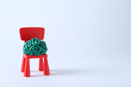 Brain made of plasticine on mini chair against white background. Space for textの写真素材
