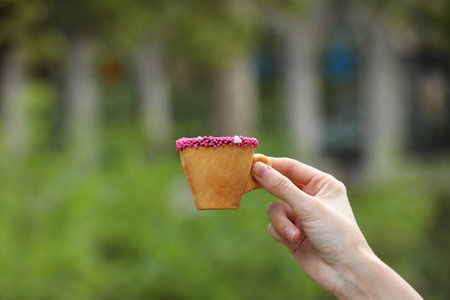 Woman holding delicious edible biscuit cup of coffee decorated with sprinkles outdoors, closeupの写真素材