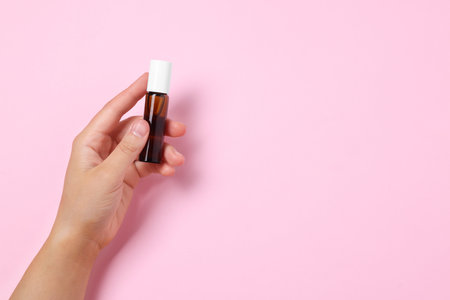 Woman with bottle of essential oil on pink background, closeup. Space for textの写真素材