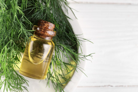 Bottle of essential oil and fresh dill on white table, top view. Space for textの写真素材