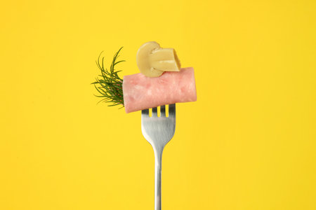Fork with tasty slice of ham, pickled mushroom and dill on yellow backgroundの写真素材