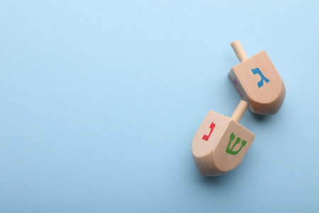 Wooden dreidels on light blue background, flat lay with space for text. Traditional Hanukkah gameの写真素材