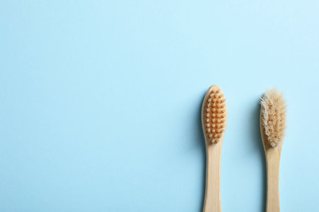 Two bamboo toothbrushes on light blue background, flat lay. Space for text