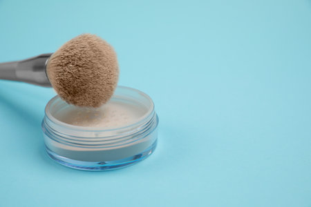 Loose face powder and brush on light blue background, space for text