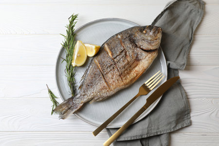 Delicious baked fish served with rosemary and lemon on white wooden table, top view. Seafoodの写真素材