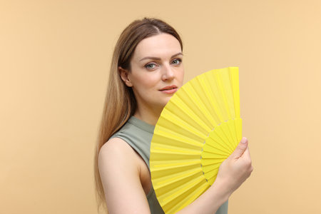 Beautiful woman with yellow hand fan on beige backgroundの写真素材
