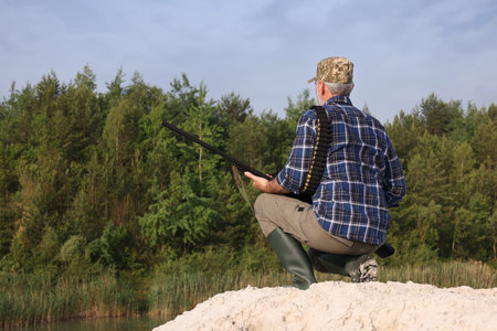Man with hunting rifle near lake outdoors, back view. Space for textの写真素材