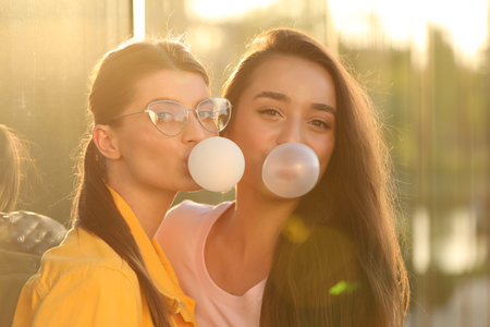 Beautiful young women blowing bubble gums outdoors on sunny dayの写真素材