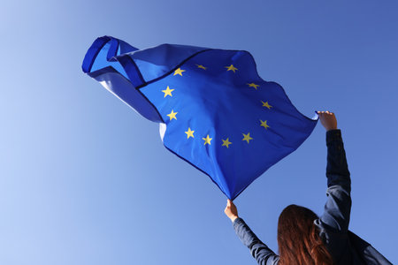 Woman holding European Union flag against blue sky outdoors, low angle viewの写真素材