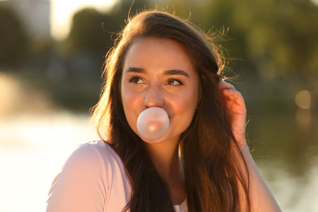 Beautiful young woman blowing bubble gum outdoorsの写真素材