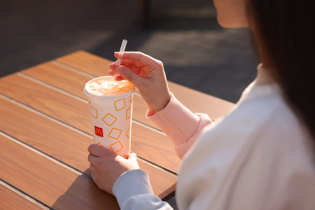 Lviv, Ukraine - September 26, 2023: Woman with McDonald's drink at wooden table outdoors, closeupのeditorial素材