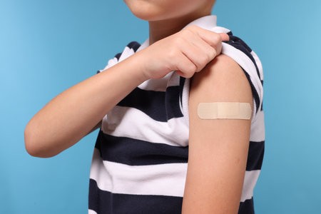 Boy with sticking plaster on arm after vaccination against light blue background, closeupの写真素材