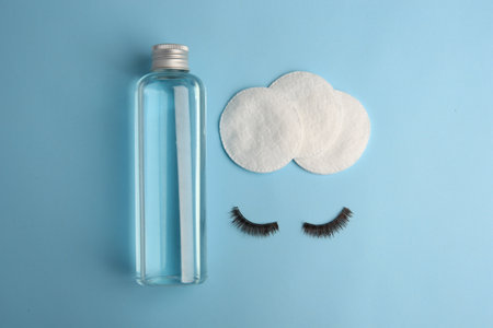 Bottle of makeup remover, cotton pads and false eyelashes on light blue background, flat layの写真素材