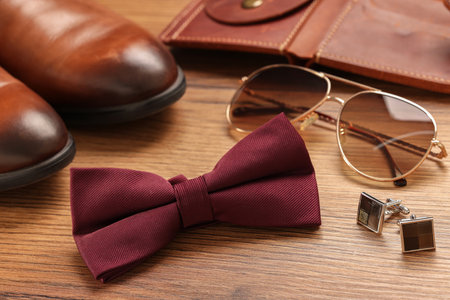 Stylish burgundy bow tie, sunglasses, shoes, brown wallet and cufflinks on wooden backgroundの写真素材