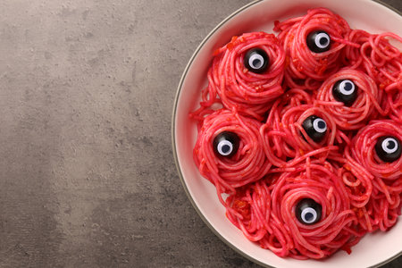 Red pasta with decorative eyes and olives in bowl on gray textured table, top view with space for text. Halloween foodの写真素材