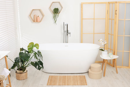 Stylish bathroom interior with bath tub, houseplants and bamboo matの写真素材