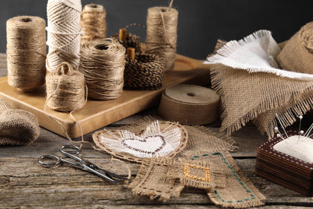 Pieces of burlap fabric, spools of twine and different sewing tools on wooden tableの写真素材