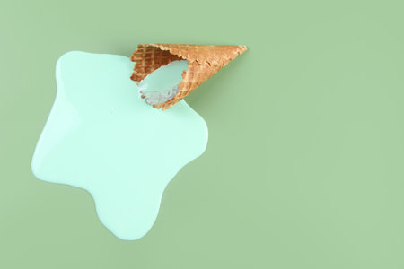 Melted ice cream and wafer cone on green background, top view. Space for textの写真素材