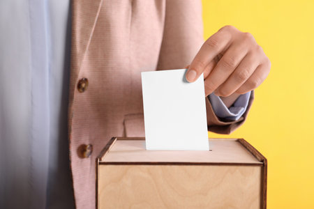Woman putting her vote into ballot box on orange background, closeupの写真素材