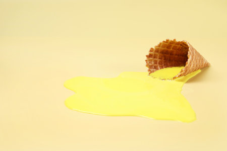 Melted ice cream and wafer cone on yellow background, space for textの写真素材
