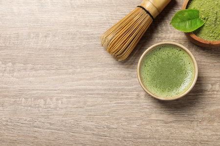 Cup of fresh matcha tea, bamboo whiskey and green powder on wooden table, flat lay. Space for textの写真素材