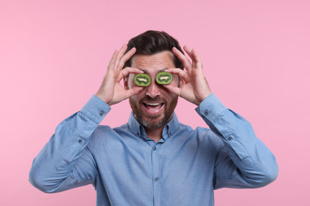 Man holding halves of kiwi near his eyes on pink backgroundの写真素材