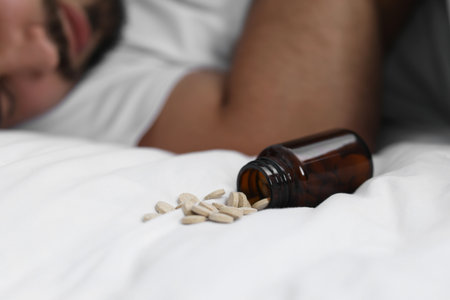 Man sleeping on bed, closeup. Overturned bottle with antidepressants, selective focusの写真素材
