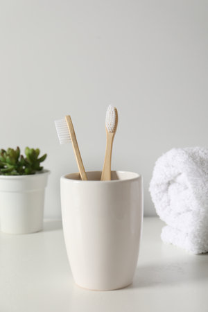 Bamboo toothbrushes in holder, potted plant and towel on white countertopの写真素材
