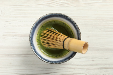 Cup of fresh matcha tea with bamboo whiskey on white wooden table, top view