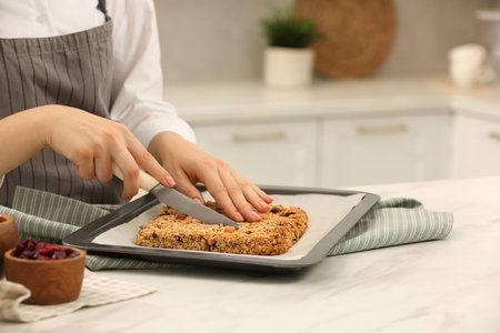 Woman cutting granola bars at table in kitchen, closeupの写真素材