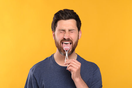 Handsome man brushing his tongue with cleaner on yellow backgroundの写真素材