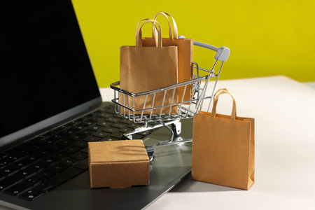 Online store. Laptop, mini shopping cart and purchases on beige table, closeupの写真素材