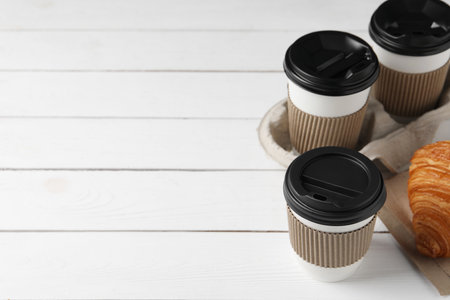 Coffee to go. Paper cups with tasty drink and croissant on white wooden table. Space for textの写真素材