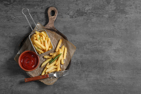 Tasty French fries, ketchup and rosemary on gray table, top view. Space for text
